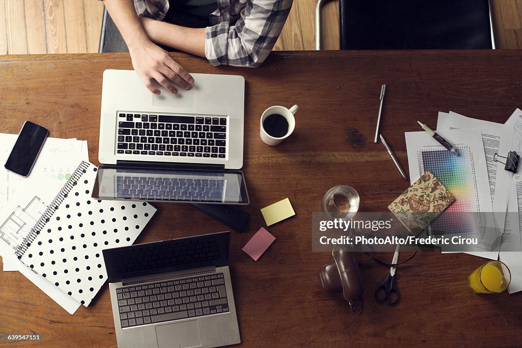 Man using laptop computer on desk cluttered with documents