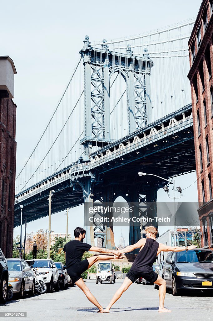 Two men leaning sideways in yoga position in front of Manhattan Bridge, New York, USA