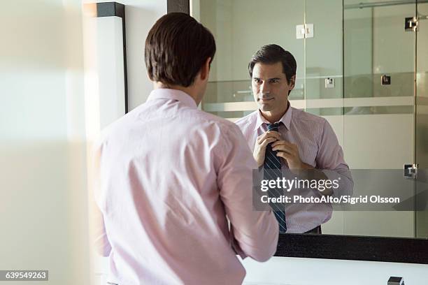 man looking in bathroom mirror, adjusting necktie - get dressed male stock pictures, royalty-free photos & images