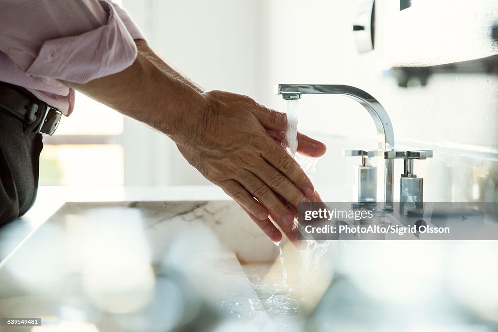 Man washing hands in bathroom sink, cropped