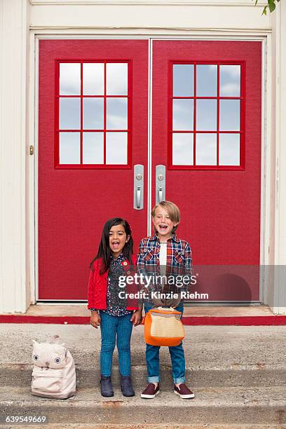 portrait of elementary schoolgirl and boy with satchels at elementary school doorway - enfant cartable photos et images de collection