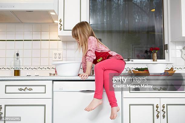 girl looking into mixing bowl whilst sitting on kitchen counter - 6 year old blonde girl stock pictures, royalty-free photos & images