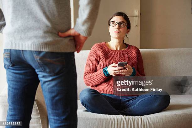 cropped shot of man in front of girlfriend on sofa with smartphone - neid stock-fotos und bilder