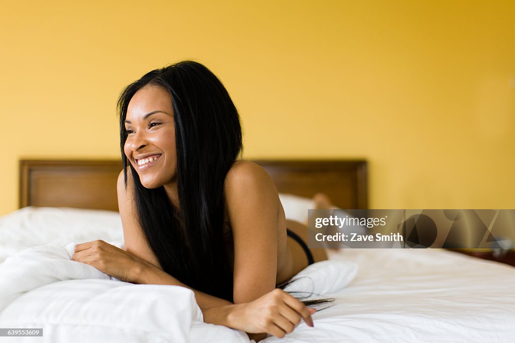 Young woman with long black hair wearing knickers lying on bed