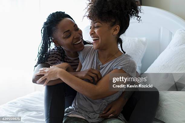 lesbian couple relaxing on bed, hugging, laughing - lesbian bed stock pictures, royalty-free photos & images