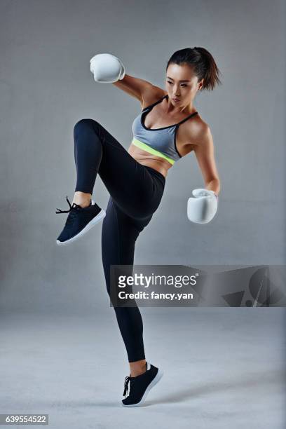 young woman in boxing gloves kicking - asian female bodybuilder stock-fotos und bilder