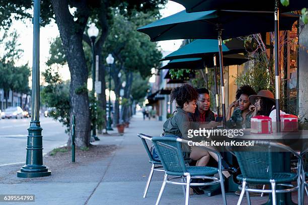 group of female friends sitting at table, outside cafe, looking at smartphone - south pasadena california stock pictures, royalty-free photos & images