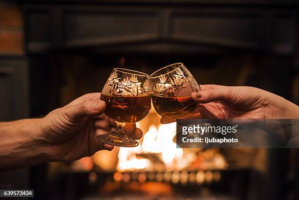 couple with two glasses of alcoholic drink  in front fireplace - whiskey stock pictures, royalty-free photos & images