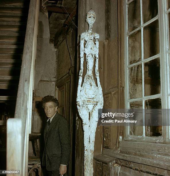 Artist Alberto Giacometti standing next to a staircase outside of his house. | Location: Giacometti's house in France..
