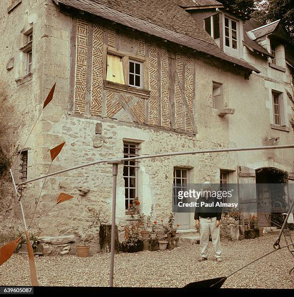 Alexander Calder standing in front of his house in Sache, France. A sculpture by Calder can be seen in the foreground. Ca. 1950-1976.