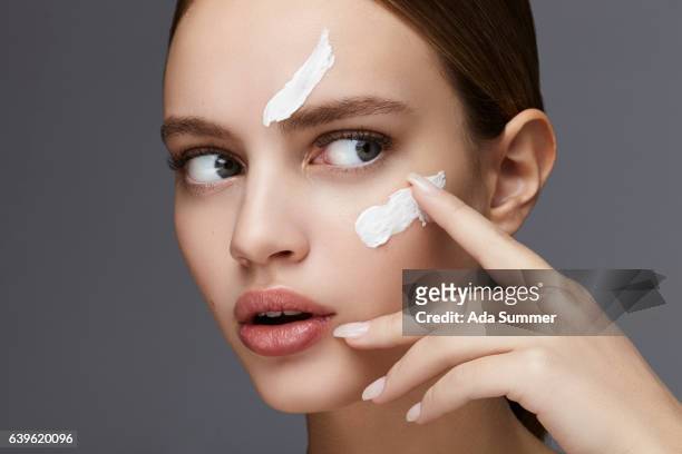studio shot of a beautiful woman applying cream on her face - beauty treatment fotografías e imágenes de stock