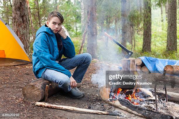 teen boy sitting by burning campfire cooking - open day 13 imagens e fotografias de stock