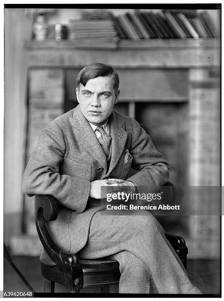 Portrait of American composer, musician, and inventor George Antheil as he sits, cross-legged, on a chair, 1920s.