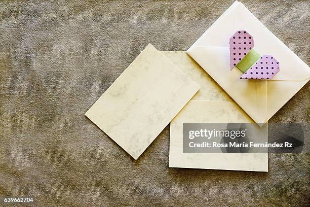 blank gretting card, enveloppe and red paper folded origami handmade heart. flat lay composition, overhead and copy space. subject captured againt soft window lighting over fabric and abstract background. - red card envelope stock pictures, royalty-free photos & images