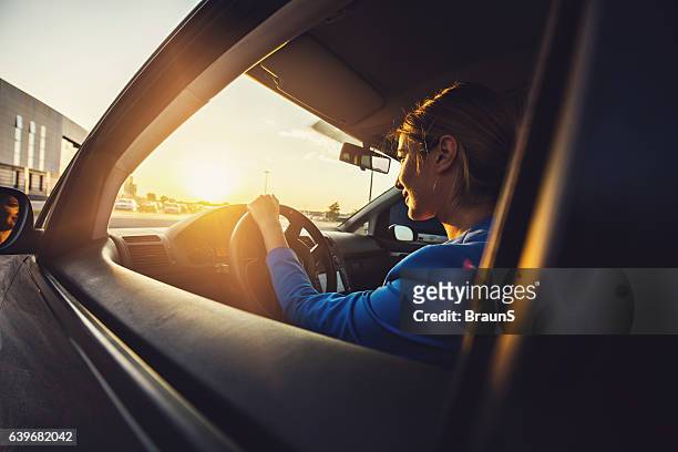 young smiling businesswoman driving a car at sunset. - driving sun stock pictures, royalty-free photos & images