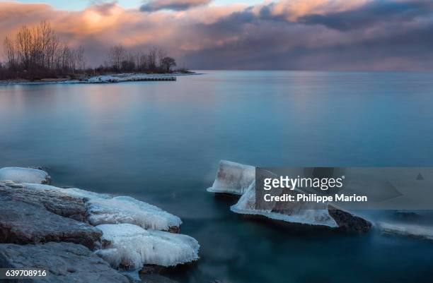 ice capped rocks on wintery lake ontario (long exposure) - ashbridge's bay, toronto - lake ontario stock pictures, royalty-free photos & images