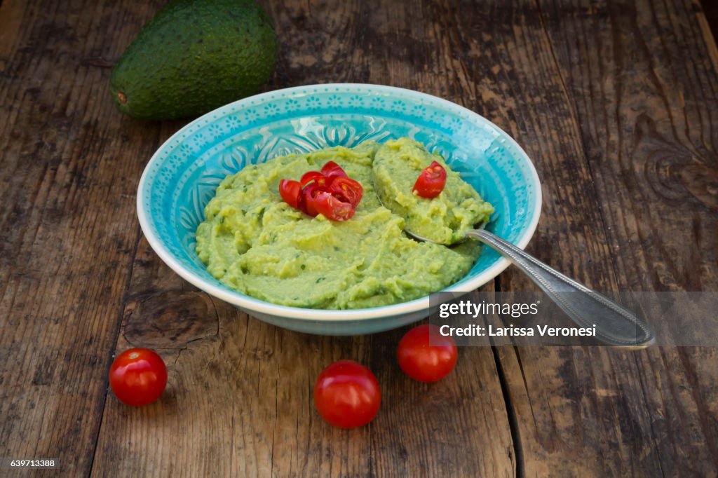 Bowl of guacamole, Avocado and Tomatoes on dark wood