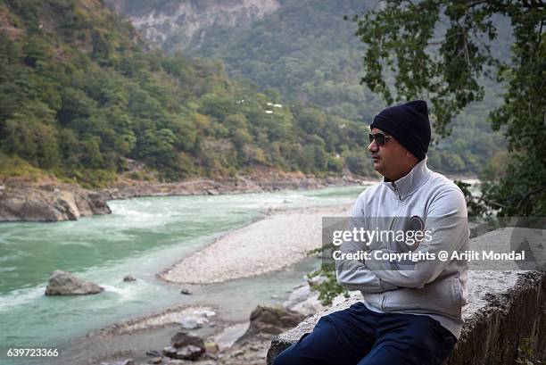 middle aged man sitting alone riverside and looking at river ganga, rishikesh - rishikesh meditation stock pictures, royalty-free photos & images