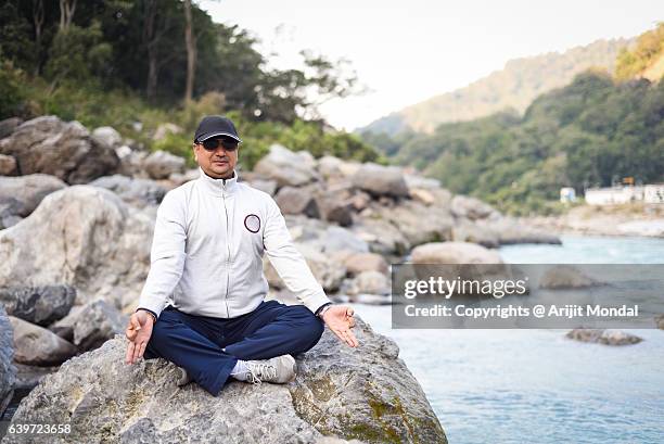 middle aged man practising meditation and yoga at riverside of ganga, rishikesh - rishikesh meditation stock pictures, royalty-free photos & images