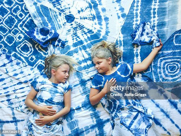 two girls lying on variety of tie dyed articles - blonde hair dye stock pictures, royalty-free photos & images