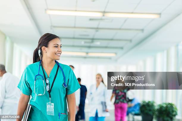 cheerful hispanic nurse walks in hospital corridor - schooldokter stockfoto's en -beelden