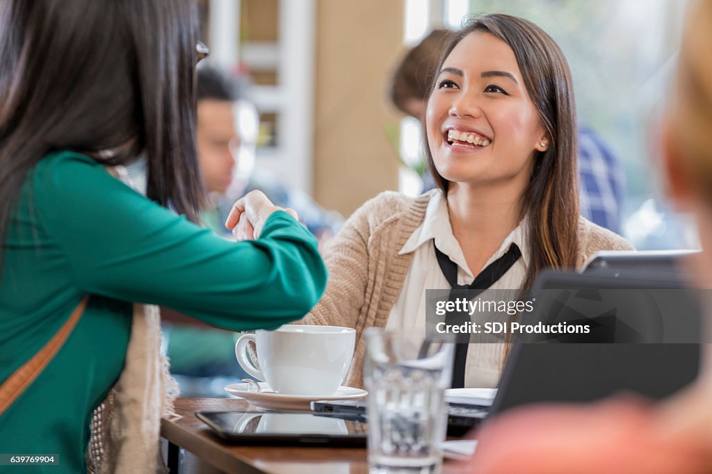 Confident businesswoman shakes colleagues hand in coffee shop