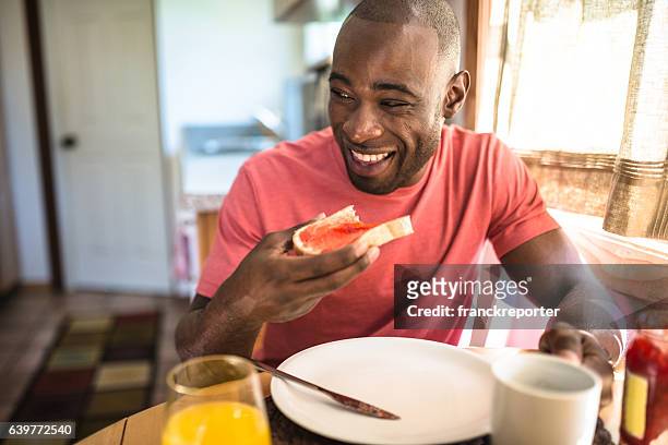 afrikanische mann tun frühstück wie zu hause fühlen. - brot mund stock-fotos und bilder