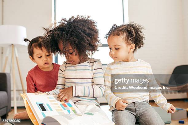 three kids in daycare with book - multilingual stock pictures, royalty-free photos & images