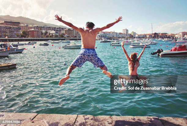 father and daughter jumping into sea in a beautiful harbor - father sun stock pictures, royalty-free photos & images