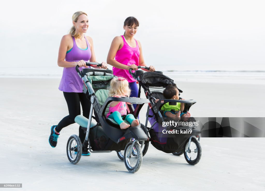 Two mothers and babies in strollers jogging on beach