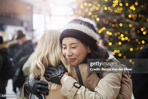 asian woman embraces friend in railroad station, christmas tree in background. - winter decoration stock pictures, royalty-free photos & images