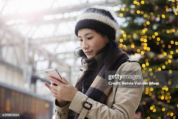 asian woman looks at her phone in railroad station. - christmas smartphone stock pictures, royalty-free photos & images