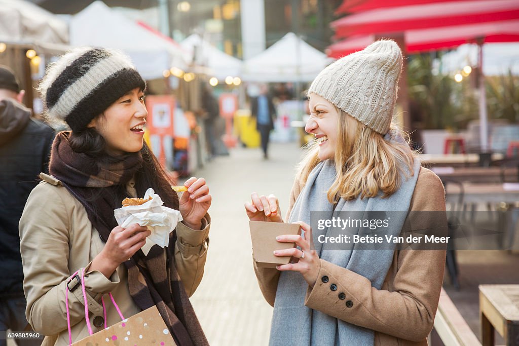 Women eating and chatting, while walking through outdoor food market.