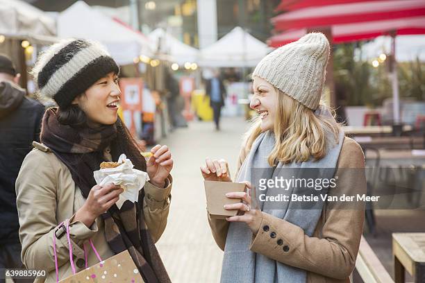 women eating and chatting, while walking through outdoor food market. - white shawl stock pictures, royalty-free photos & images