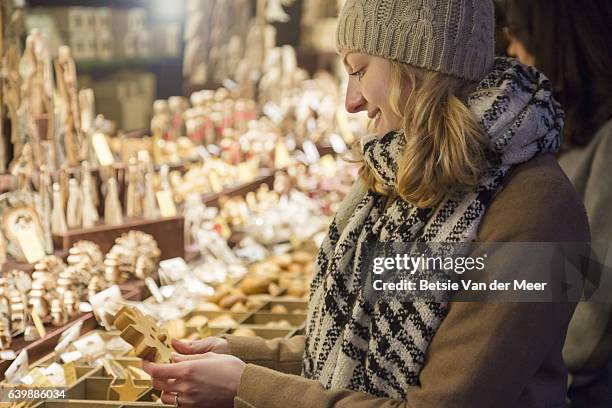 woman looks at wooden christmas decoration at christmas market stall. - city breaks winter stock pictures, royalty-free photos & images
