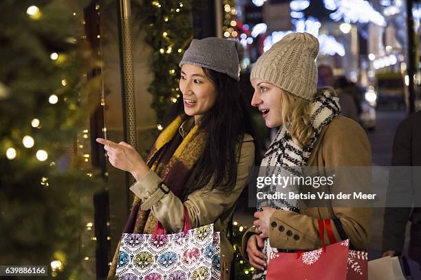 female friends are looking into shopwindow while carrying christmas shopping bags. - blonde english woman shopping foto e immagini stock