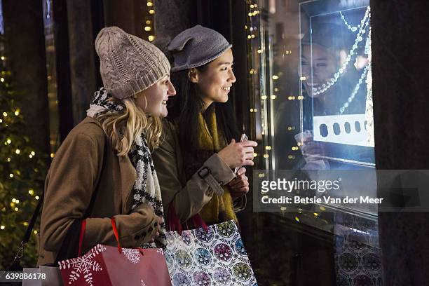 female friends are looking into jewelry shop window at night time. - sombrero de fiesta fotografías e imágenes de stock