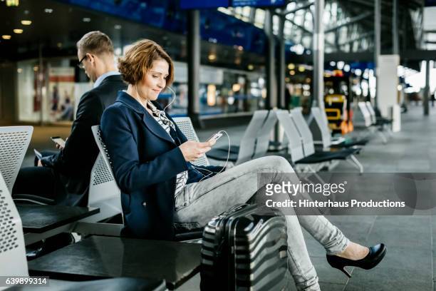 mature businesswoman waiting at the airport while using a smart phone - white bench stock pictures, royalty-free photos & images