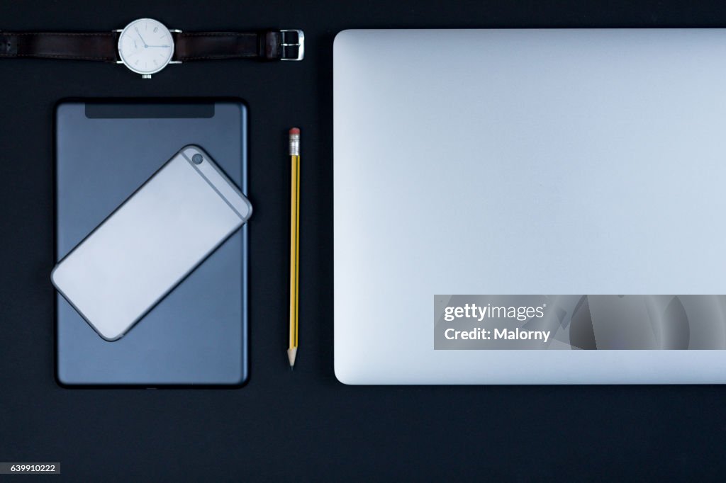 Laptop, smart phone, watch, pencil on black background, high angle view, flat lay, knolling, overhead, top view