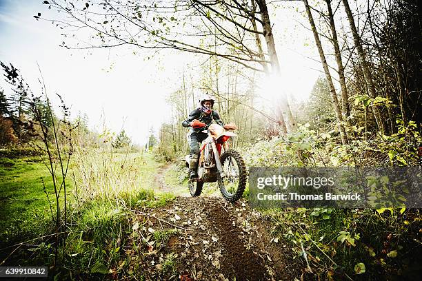 female motorcyclist riding over jump on forest trail on fall afternoon - corrida de motos imagens e fotografias de stock