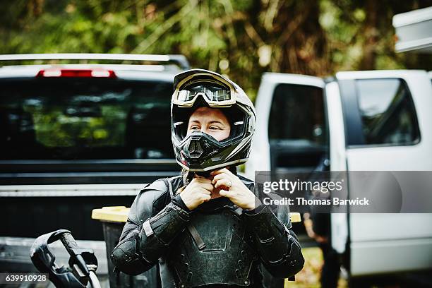 female motorcyclist putting on helmet before riding dirt bike with friends - motocross stock photos et images de collection