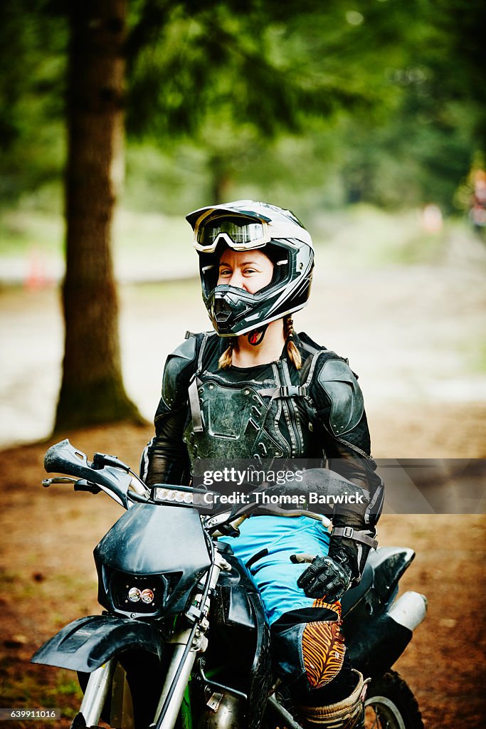 Smiling female motorcyclist sitting on dirt bike before riding with friends