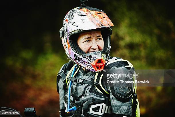smiling female motorcyclist with muddy face in discussion with friends while riding dirt bike - motocross foto e immagini stock
