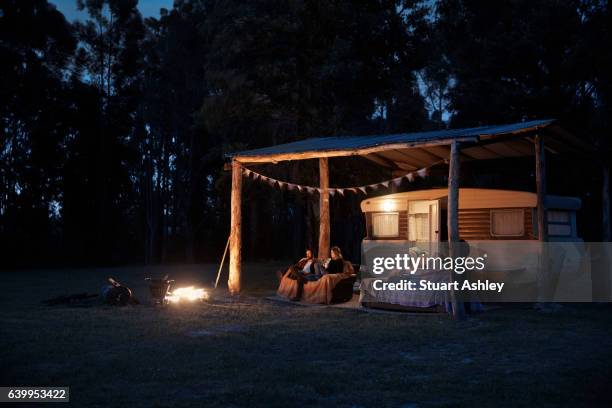 man and woman couple sitting by caravan and fire at night - camping couple stock pictures, royalty-free photos & images