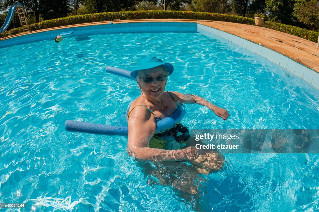 A Senior lady exercising with a noodle float in a swimming pool.