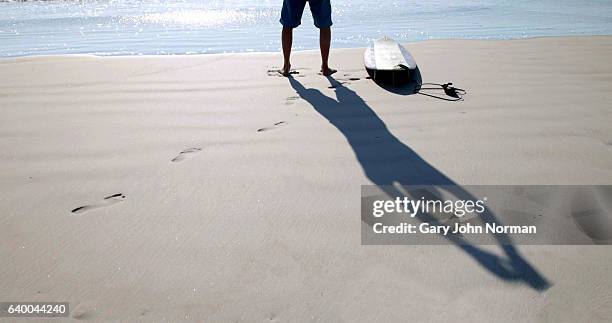 shadow of male surfer stretching his body by the water edge - sombra en primer plano fotografías e imágenes de stock