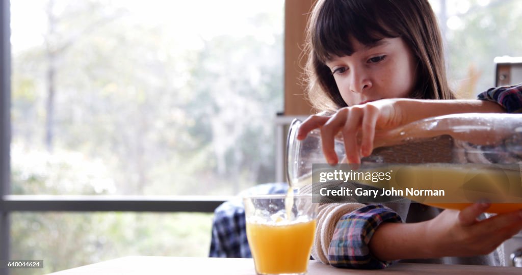 Girl pouring fresh orange juice into glass in kitchen.