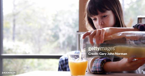 girl pouring fresh orange juice into glass in kitchen. - orange juice stock pictures, royalty-free photos & images