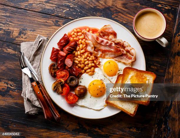 english breakfast with fried eggs, sausages, bacon, beans, toasts and coffee on wooden background - gevuld stockfoto's en -beelden