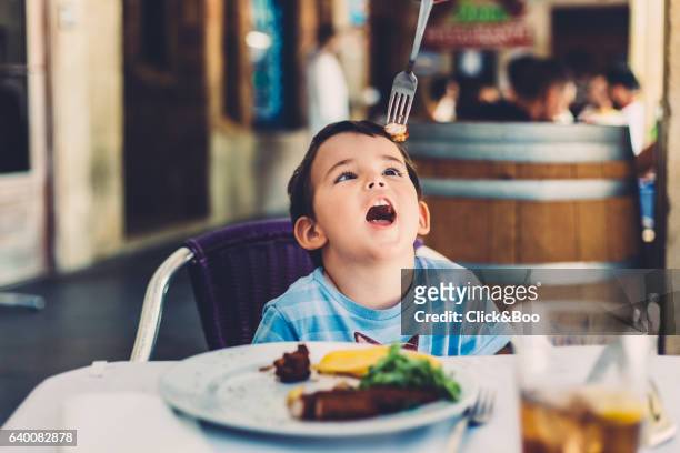 little boy in a restaurant playing with a fork - ojos marrones stock-fotos und bilder
